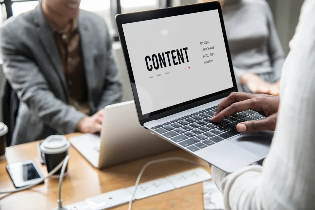 Pessoa trabalhando em um laptop com uma tela mostrando o termo "CONTENT" e palavras-chave relacionadas ao marketing digital, como "Efficient", "Searchable", "Accessible" e "Intuitive".