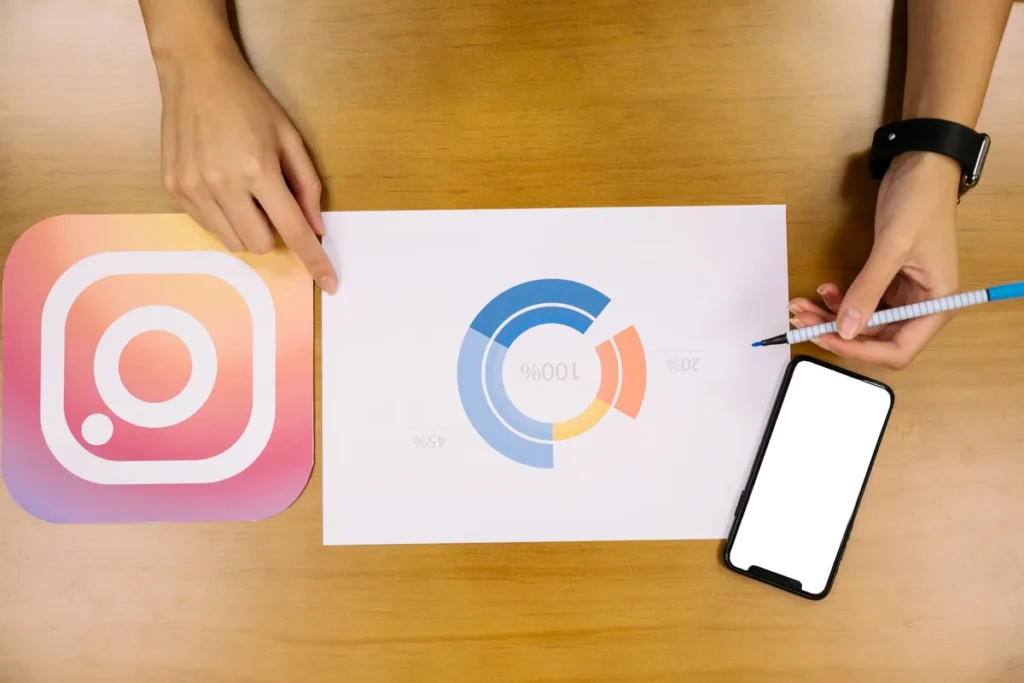 Mãos analisando gráfico de desempenho com logotipo do Instagram, celular e caneta sobre mesa de madeira.