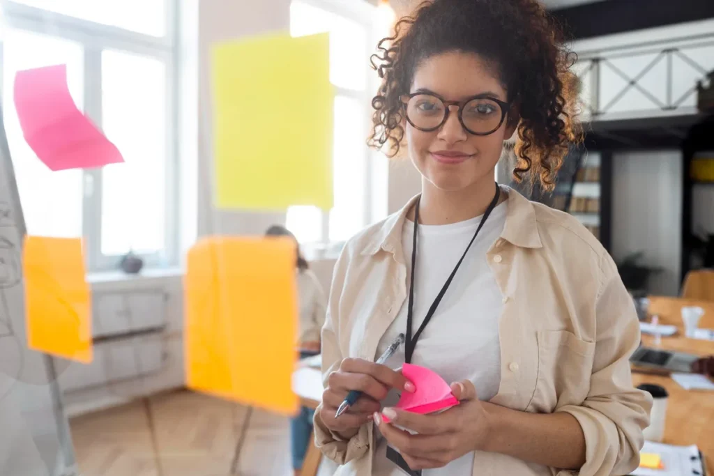 Jovem profissional sorrindo em escritório moderno com post-its coloridos em um brainstorming criativo.