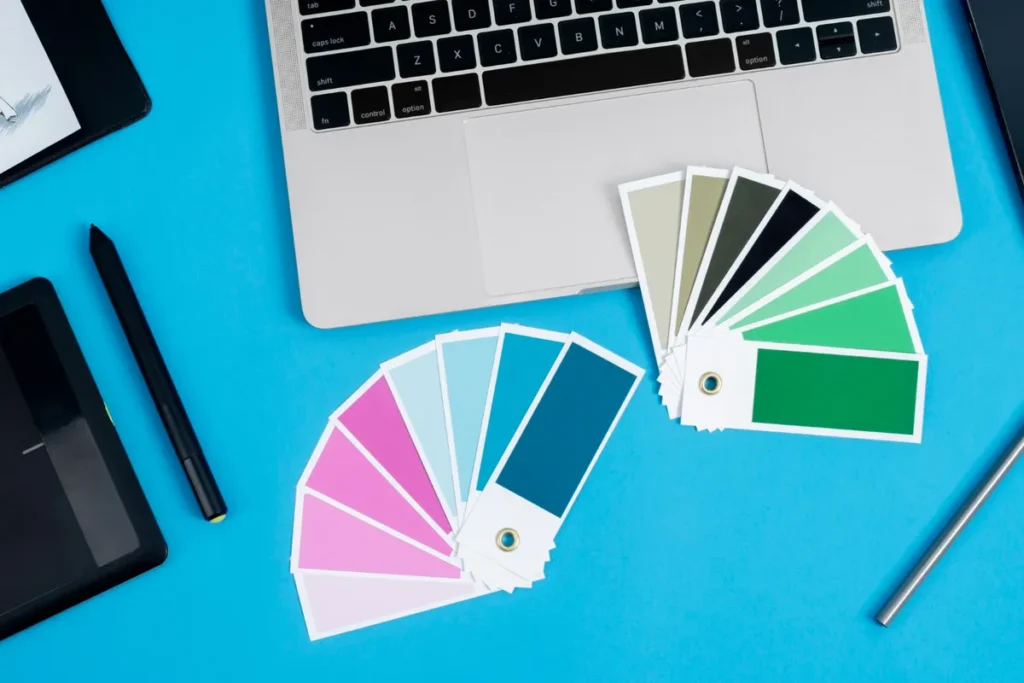 Cartelas de paletas de cores organizadas ao lado de um notebook prateado sobre uma mesa azul, representando processo criativo de design gráfico, escolha de identidade visual ou branding
