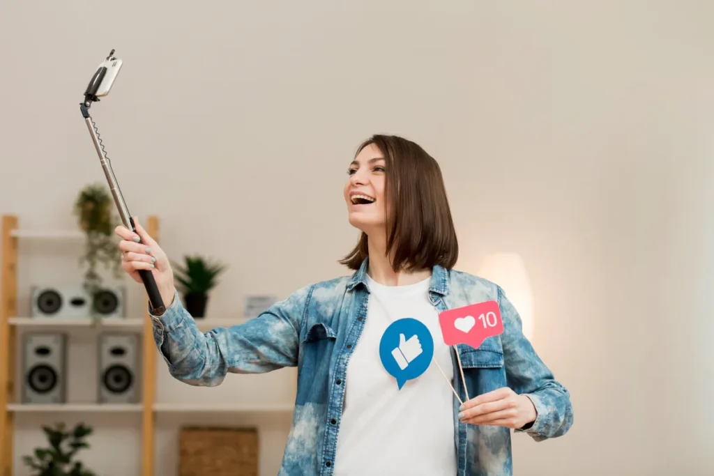 Mulher sorridente segurando bastão de selfie e placas com ícones de curtida e like em ambiente moderno