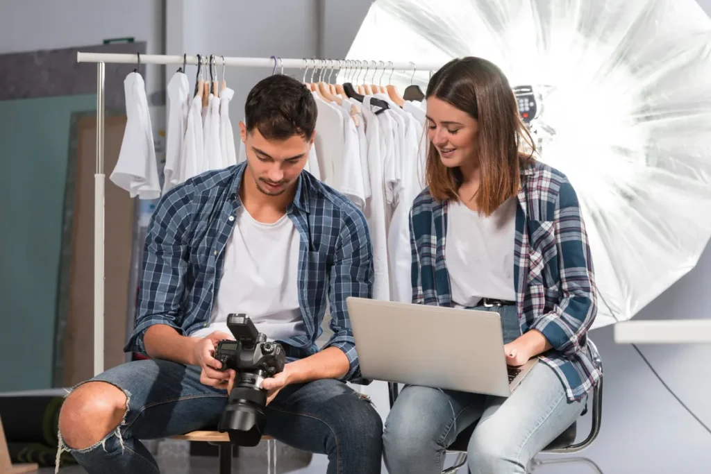 Dois jovens em um estúdio com câmera e laptop, representando criadores de conteúdo digital focados em fotografia e edição de mídias sociais.
