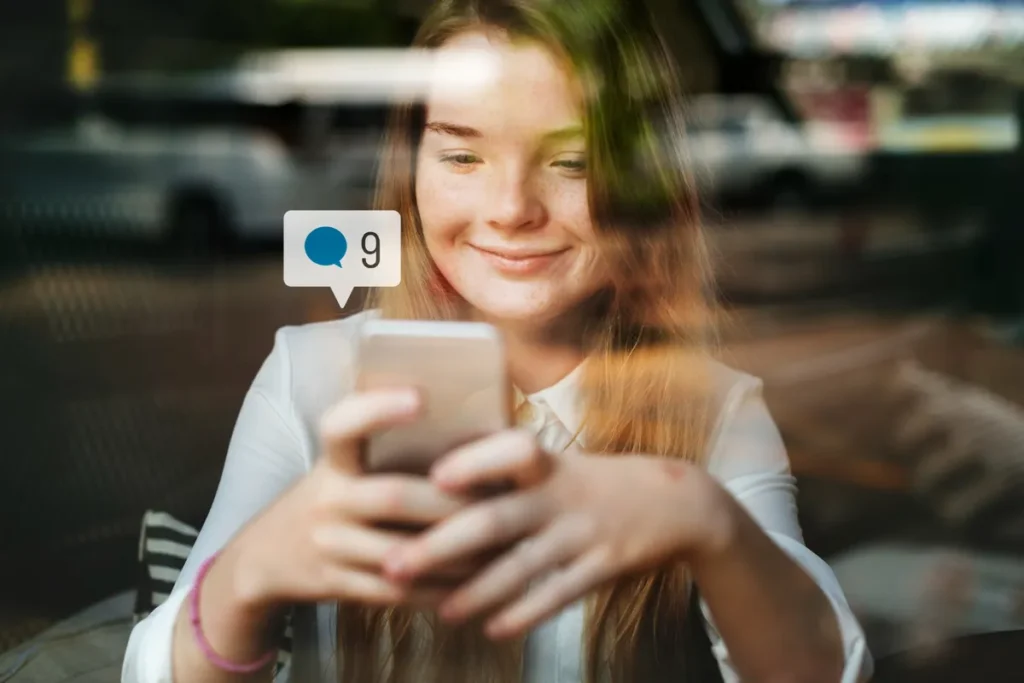 Mulher sorridente olhando para um smartphone com uma notificação de mensagem, ilustrando a comunicação digital e a importância de usar palavras-chave.