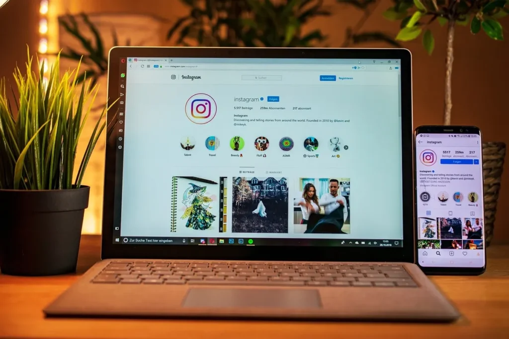 Tela de um laptop e de um smartphone exibindo a interface do Instagram, com plantas decorativas ao redor.