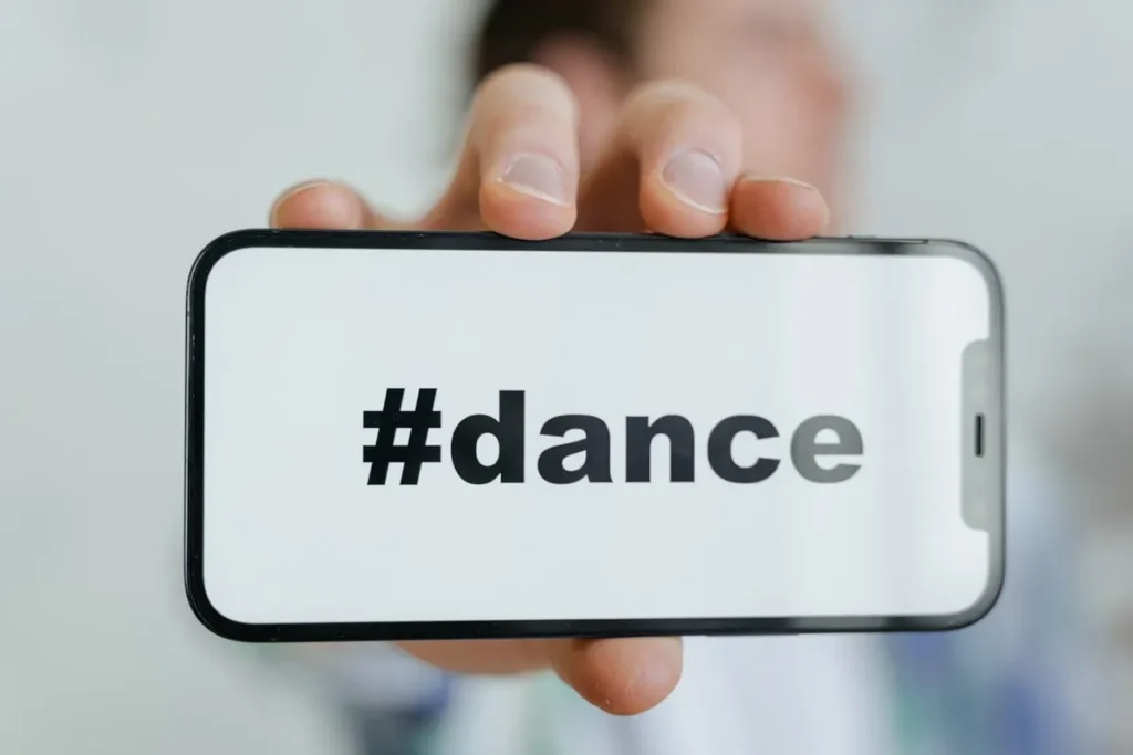 Pessoa segurando um celular horizontalmente com a hashtag #dance em letras pretas sobre um fundo branco, representando conteúdo de dança para visualizações em stories.