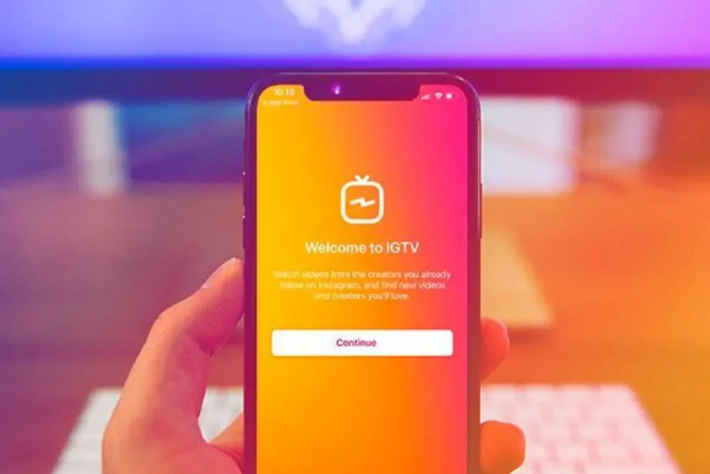 Mão segurando um smartphone que exibe a tela de boas-vindas do IGTV. O fundo da tela é um degradê colorido e o texto "Welcome to IGTV" aparece com o logo da plataforma, um botão de "Continue" e uma breve descrição da funcionalidade.