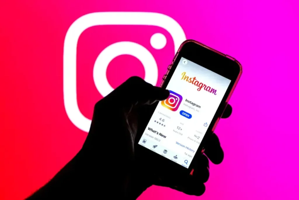 Uma mão segura um celular com a página de download do Instagram na tela. No fundo, um grande logotipo do Instagram é projetado. A imagem sugere o uso de heatmap para analisar o engajamento e a interação dos usuários com o aplicativo.