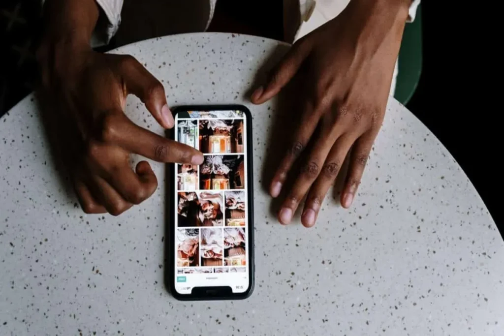 legendas para fotos Instagram, uma pessoa olhando para a tela de um celular com um feed de fotos do Instagram em uma mesa de pedra, com as duas mãos visíveis, tocando na tela.