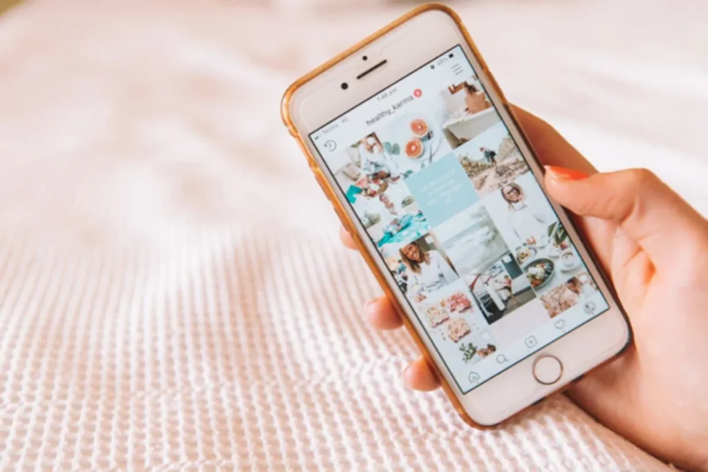Uma pessoa segurando um celular com o feed do Instagram do perfil "@healthy_karma", ilustrando a importância da comunicação visual e do tom de voz de uma marca.