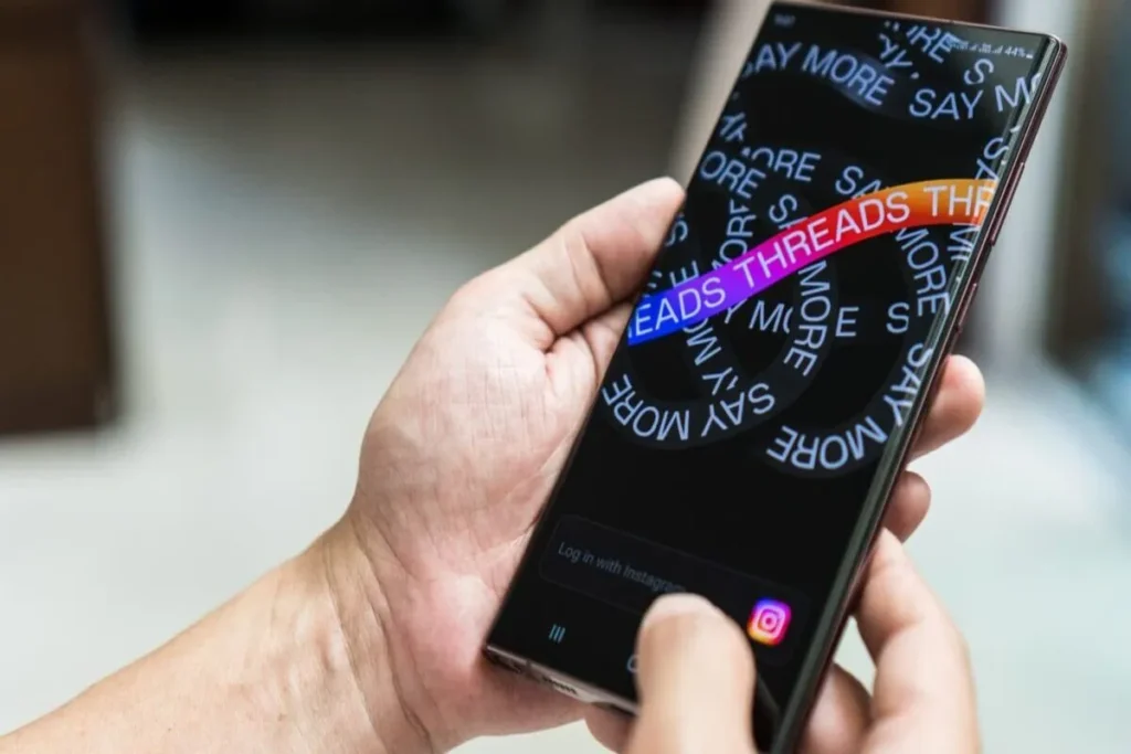 Pessoa segurando smartphone com a tela do aplicativo Threads do Instagram, destacando o login e a interface inicial.