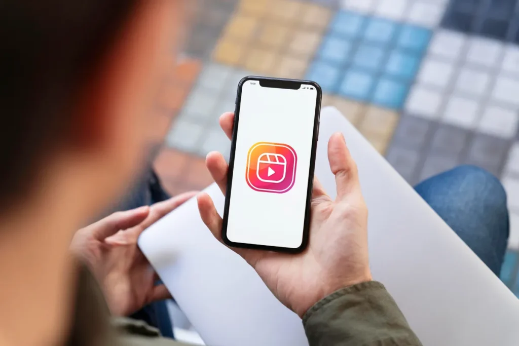 Pessoa segurando um smartphone com o ícone do Instagram Reels na tela, representando o conteúdo de vídeo na plataforma.