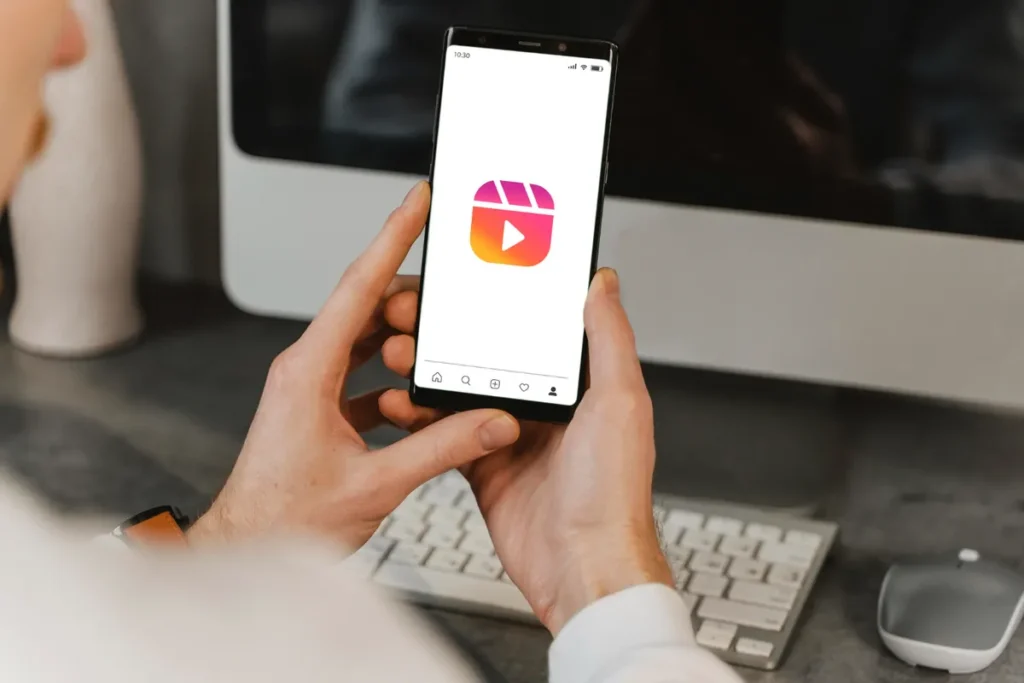 Pessoa segurando um smartphone com o ícone do Instagram Reels na tela, representando a busca por música para Reels em alta.