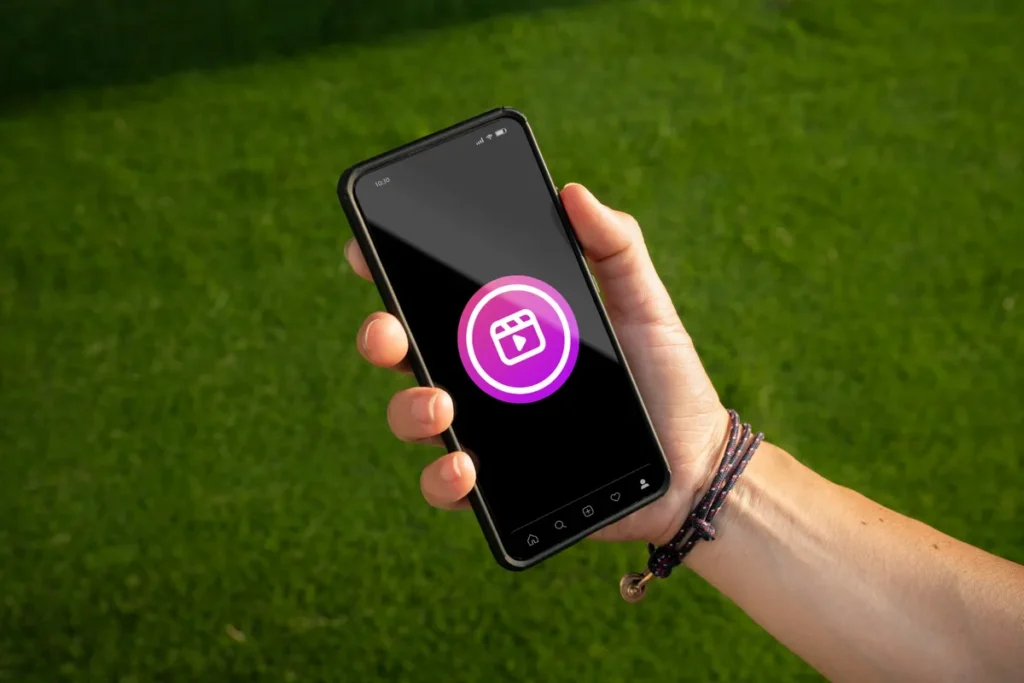 Mão segurando smartphone sobre a grama, com o ícone do Instagram Reels em destaque, simbolizando a criação de conteúdo com música para Reels ao ar livre.