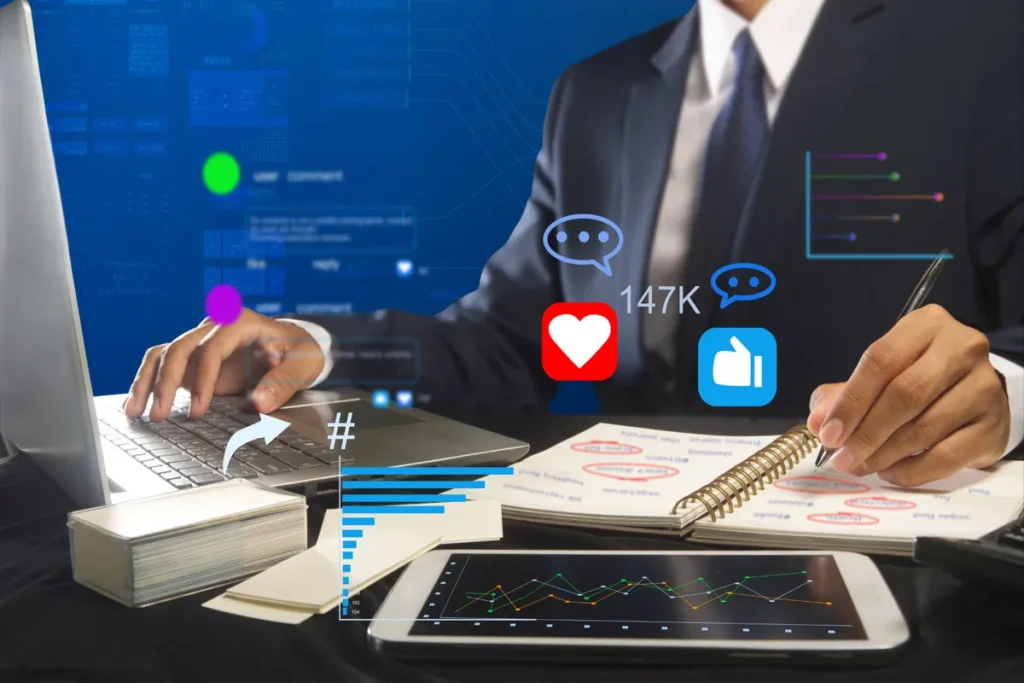 Profissional de marketing em uma mesa com notebook, tablet e anotações, interagindo com ícones de mídias sociais e gráficos flutuantes. Cena de análise de dados e social listening.
