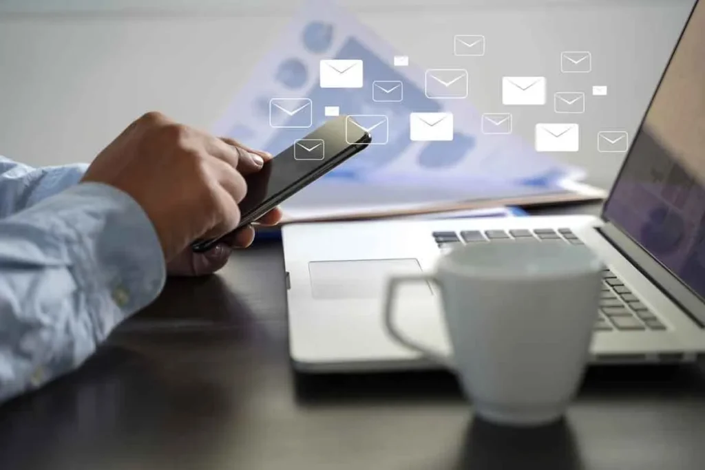 Profissional usando celular e notebook para enviar e receber mensagens, representando estratégias de social selling e engajamento digital.