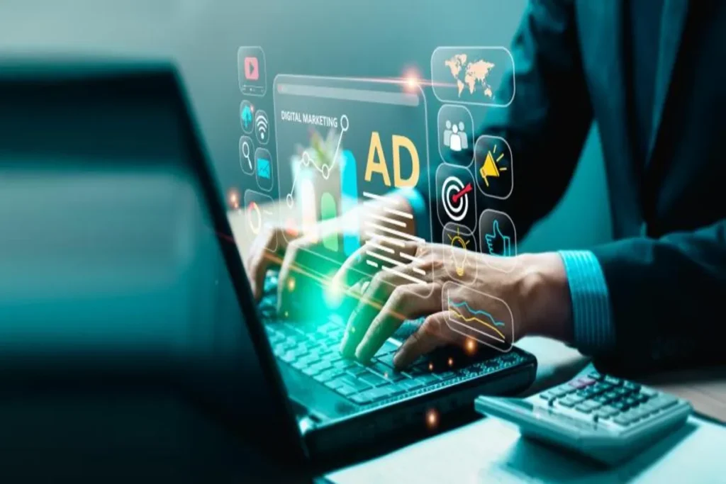 Mãos de uma pessoa digitando em notebook, com projeções holográficas de ícones e gráficos de marketing digital, incluindo um símbolo de "AD", alvo e um mapa-múndi. Cena de tráfego pago.